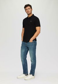 Czarna koszulka polo z krótkim rękawem, zestawiona z niebieskimi dżinsami. Całość dopełniają białe trampki. Prosty i swobodny design.