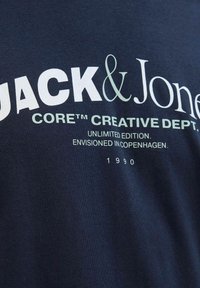 Marineblå bomulds t-shirt med fed hvid tekst: "JACK & JONES," med accenter. Designet inkluderer "CORE™ CREATIVE DEPT." og året "1990."