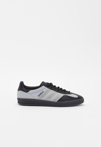 Fekete és szürke sneaker, hálós és szintetikus bőrből készült. Három vízszintes csíkkal és gumitalppal rendelkezik. Modell neve: Gazelle.