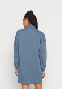 Vestido de mangas longas, com colarinho, em tecido azul claro. Corte descontraído, até à metade da coxa, com bainha reta. Textura suave e detalhes mínimos.