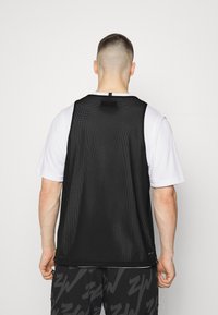 Svart nät utan ärm med rund hals, med ett mjukt vitt underlager och en liten svart etikett på baksidan.