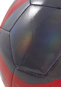 Pallone da calcio con una superficie nera testurizzata, dettagli rossi e un motivo a puntini. I pannelli esagonali sono cuciti insieme.