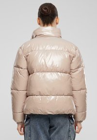 Puffjakke i skinnende lys beige, med høy krage, quiltede seksjoner, elastiske ermer og en boksformet silhuett.