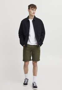 Fekete gombos ing, fehér póló, olivazöld rövidnadrág, fekete sportcipő fehér talppal, fehér bokazoknival kiegészítve. Minta nélkül.