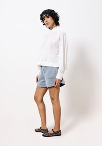 Weiß geblümte Bluse, helle Jeansshorts und schwarze Ballerinas mit Leopardenmuster. Strukturiertes Stoffdetail und knopfüberzogene Manschetten an der Bluse.