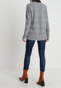 Grå långärmad topp med svart krage, matchad med mörkblå jeans och glänsande orange ankelstövlar med tjock svart klack.