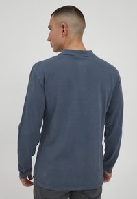 Langermet polo i marineblå, laget av teksturert stoff. Har en klassisk krage og sidesplitter for komfort. Enkelt, uten pryd.