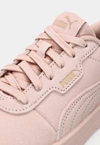 Αθλητικά παπούτσια Puma σε απαλό ροζ σουέντ με κορδόνια στο ίδιο χρώμα, διακοσμημένα με χρυσές λεπτομέρειες λογότυπου και ανάγλυφη σόλα. Στρογγυλεμένη μύτη και ομαλές γραμμές.
