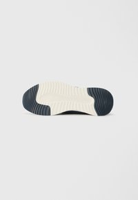 Semelle de chaussure présentant une texture en caoutchouc avec un motif en vagues de couleur bleu foncé et beige, offrant ainsi de l'adhérence et de la durabilité. Design antidérapant visible.
