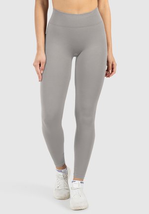 Graue, hochtaillierte Leggings aus dehnbarem Stoff, mit glatter Textur und figurbetontem Design, kombiniert mit weißen Sportschuhen.