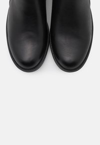 Stivali alla caviglia in pelle nera con una texture liscia, punta arrotondata e cuciture a contrasto lungo la suola. Design minimalista senza decorazioni.