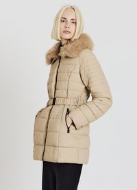 Veste matelassée beige avec col doublé de fourrure, taille ceinturée, motif matelassé et poches zippées. Texture douce et design chaud.