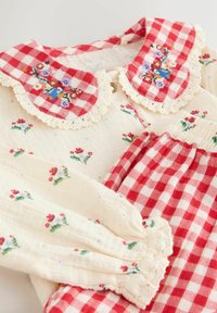 Floral-printed cream cotton top with red gingham collar, lace trim, and matching pants with a similar pattern. Soft texture, gathered cuffs.