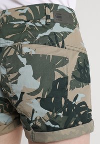 Kraťasy s kamuflážním vzorem v zelené a béžové barvě, s ohrnutým lemem, zadní kapsou a koženou nášivkou s logem na pásku.