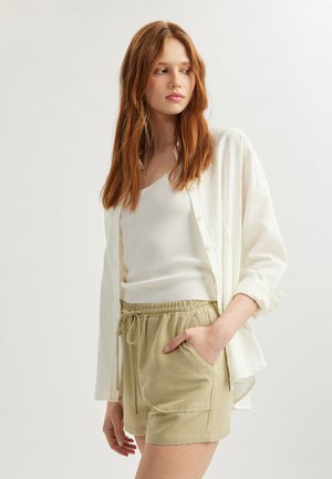 Hvid, knappet skjorte over en hvid ribbet tanktop, parret med lyse beige, snoretræks shorts med sidelommer. Glat tekstur.