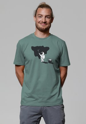 Green cotton t-shirt with short sleeves, featuring a white astronaut graphic painting a black starry sky on the front.
