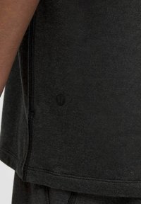 Maglietta atletica nera a maniche corte, texture liscia, cuciture piatte e un piccolo logo discreto vicino all'orlo.