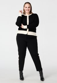 Zwart-crèmekleurig vest met een ronde hals en knoopsluiting, gecombineerd met zwarte broek met crèmekleurige accenten aan de zijkant en enkellaarsjes.