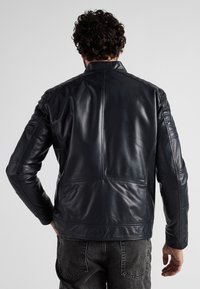 Svart läderjacka med en slät yta, kviltade axeldetaljer och ståkrage. Har en skräddarsydd passform och minimala sömdetaljer.