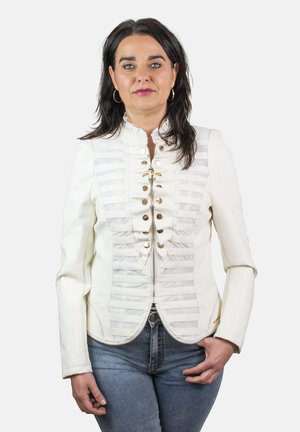 Chaqueta blanca a medida con rayas horizontales, botones dorados y un diseño ajustado. Se lleva sobre un vaquero azul. Textura suave y forma estructurada.