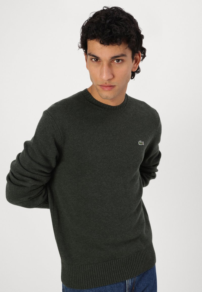 Dunkelgrüner Pullover aus strukturiertem Strick, runder Ausschnitt, gerippte Bündchen und Saum, mit kleinem gesticktem Logo auf der Brust.