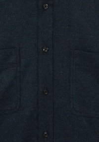 Donkerblauwe flanellen shirt met een gestructureerde afwerking, voorzien van een knoopsluiting aan de voorkant, twee borstzakken en zwarte knopen.