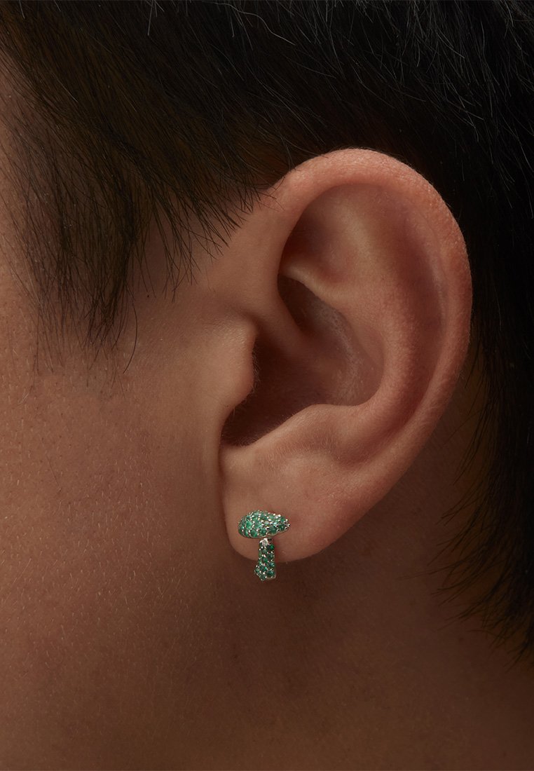 Emerald zaļš, sēņu formas stud auskars ar mirdzošiem akcentiem, novietots uz ādas tonis fona blakus ausij.
