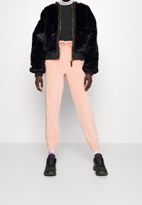 Svart fuskpäls bombarjacka, grå topp, ljusrosa sweatpants med dragsko och svarta sneakers. Enkelt design med elastiska manschetter.