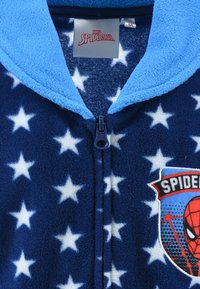 Blue fleece onesie with white stars, featuring a zipper and a Spider-Man logo patch on the front. Soft texture, cozy design.