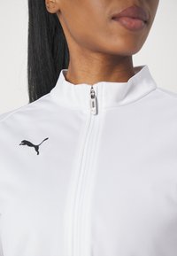 White athletic jacket with a zip closure. Features a high collar and black Puma logo on the left side. Smooth texture and fitted design.