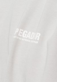 Hvit bomulls t-skjorte med "PEGADOR"-logo trykt i hvit tekst, med "CERTIFIED AUTHENTIC STREETWEAR" under i mindre bokstaver.