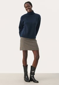 Marineblå strikket turtleneck sweater med ribbet kant, parret med en brun ternet miniskørt og sorte knæhøje støvler. Glatte teksturer gennem hele outfittet.