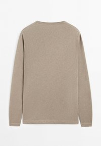 Chemise beige à manches longues et col rond, posée à plat, montrant le dos avec un design simple, uni et sans motifs ni logos visibles.