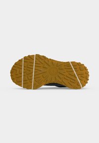 Semelle d'une chaussure jaune à semelle en caoutchouc avec des sculptures géométriques et deux lignes horizontales blanches sur fond uni clair.
