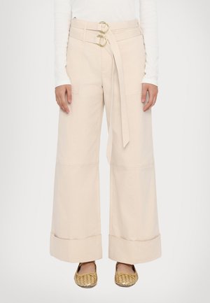 Pantalons larges en coton beige clair avec une taille haute, dotés d'une ceinture à double anneau et de bas de pantalon à revers. Fini texturé avec poches latérales.