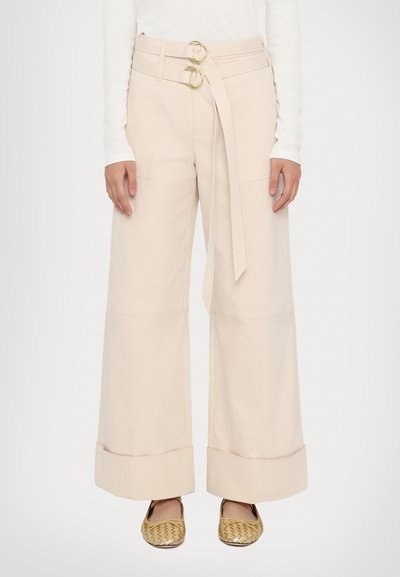 Pantaloni a gamba larga in cotone beige chiaro con vita alta, dotati di cintura a doppio anello e orli con risvolto. Finitura testurizzata con tasche laterali.
