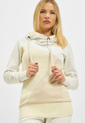 Lys beige hettegenser laget av myk, flekkete stoff. Har en cowl-hals med snor, diagonalt fargeblokkdesign og lange ermer.