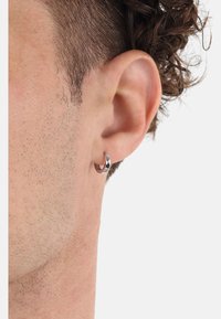 Pendiente de aro plateado en la oreja, con un acabado pulido y un ligero diseño retorcido, que muestra una apariencia elegante y moderna.