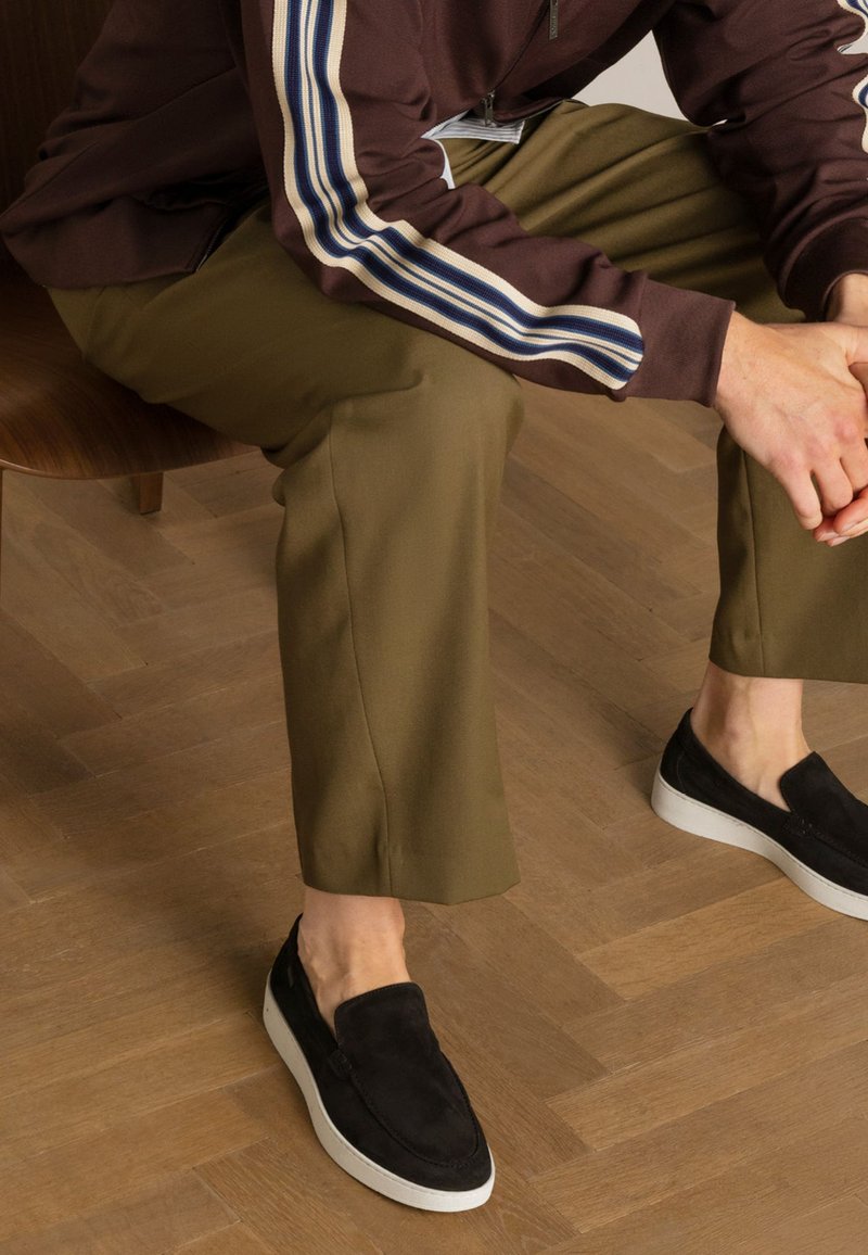 Zwarte instapschoenen met een suede afwerking en witte rubberen zolen. Olivegroene broeken met een rechte snit en een gladde textuur.
