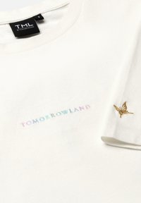 Witte katoenen t-shirt met pastel geborduurde tekst "TOMORROWLAND" en een klein gouden vlinderembleem nabij de mouw.