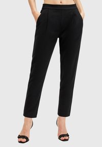 Pantaloni neri su misura con elastico in vita, due tasche laterali e una silhouette affusolata. Indossati con sandali neri con tacco.