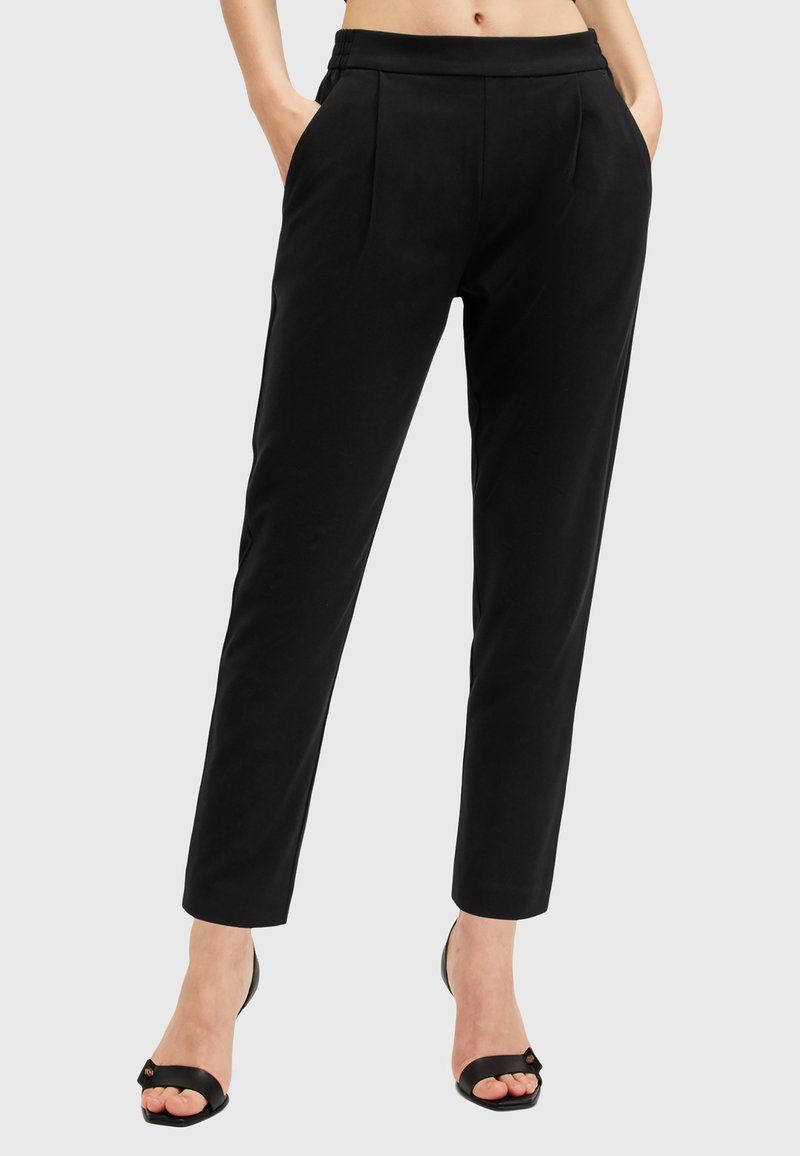 Pantaloni neri su misura con elastico in vita, due tasche laterali e una silhouette affusolata. Indossati con sandali neri con tacco.