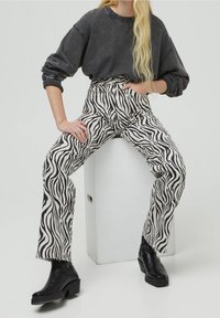Pantalon à imprimé zébré noir et blanc à taille haute, ourlets effilochés, associé à un sweat-shirt gris oversize et des bottes à talons noires.