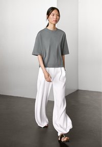 Grå oversize t-shirt med korte ærmer, parret med løse hvide bukser. Activfit-stof med en glat tekstur. Skoene har et minimalistisk design.