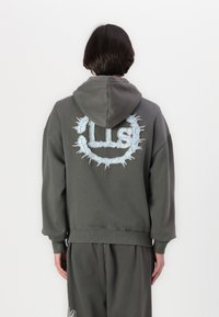 Sweatshirt cinza de algodão com um grande gráfico azul nas costas, com bordas dentadas e um bolso canguru. Inclui um capuz com cordão ajustável.