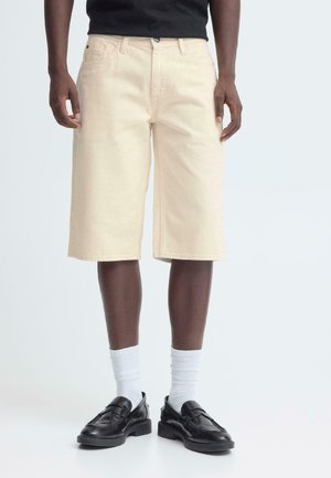 Beige denimshorts med sidelommer og et lige ben-design. Kombineret med sorte loafers og hvide crew-sokker.