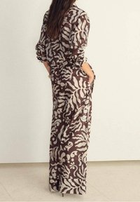 Robe longue fluide en brun et crème avec un motif abstrait, dotée de manches longues, d'une taille cintrée et de poches latérales.