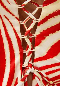 Tissu rayé rouge et blanc avec un design à lacets au niveau de l'encolure, présentant des accents noués et une texture lisse.