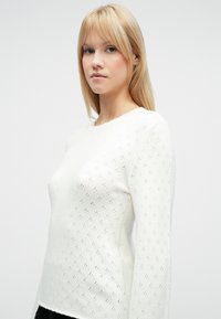 Pull blanc en tricot avec un motif texturé comprenant de petits losanges, manches longues et encolure ronde. Matière douce et légère.