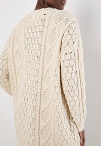 Cremefarbener Strickcardigan mit strukturierten Zopfmustern und offenen Maschen. Locker geschnitten, mit einem runden Ausschnitt und gerippten Bündchen.
